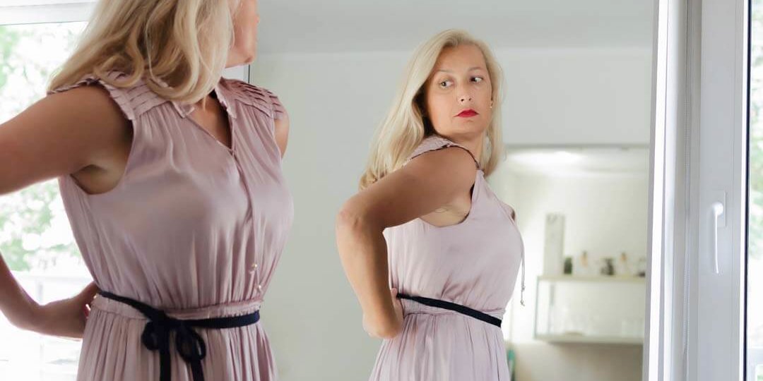 Downsize Breast Implants – Tannan Plastic Surgery woman in pink dress looking in mirror
